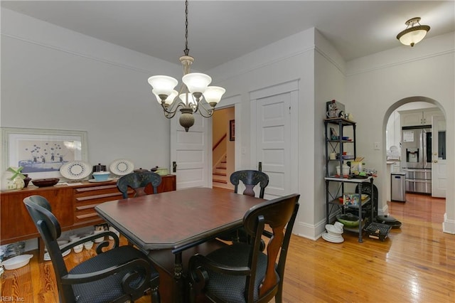 dining room with arched walkways, light wood-type flooring, stairs, and a notable chandelier