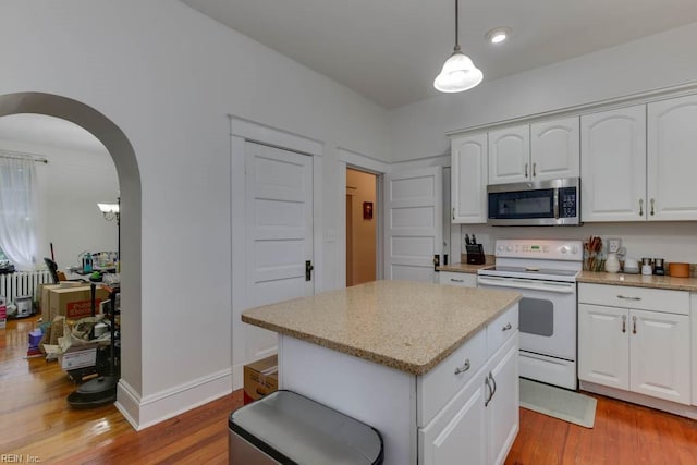 kitchen with white electric stove, arched walkways, stainless steel microwave, wood finished floors, and white cabinetry