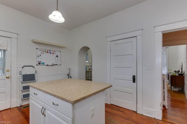 kitchen with arched walkways, a center island, white cabinetry, and wood finished floors