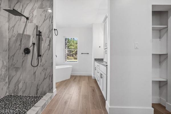 bathroom featuring vanity, wood finished floors, baseboards, a marble finish shower, and a soaking tub