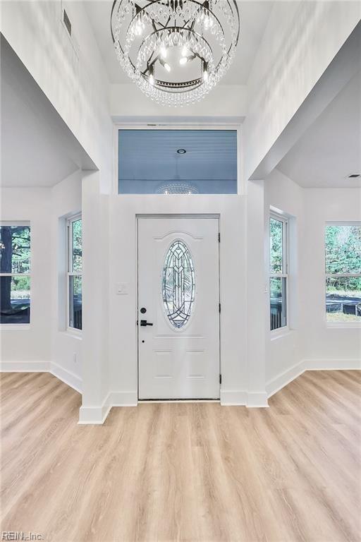 entryway with a wealth of natural light, light wood-type flooring, baseboards, and an inviting chandelier