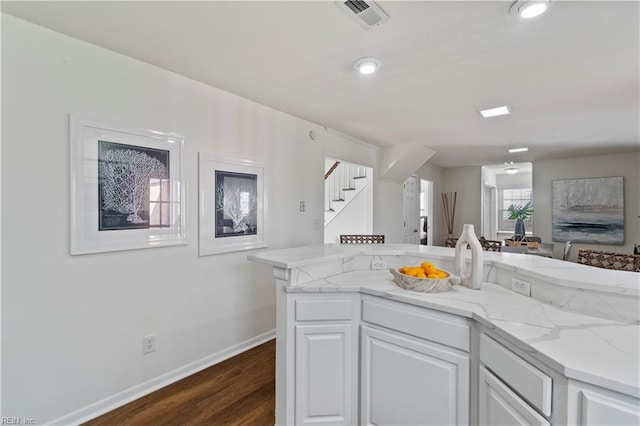 kitchen with light stone counters, dark wood-type flooring, visible vents, and white cabinetry
