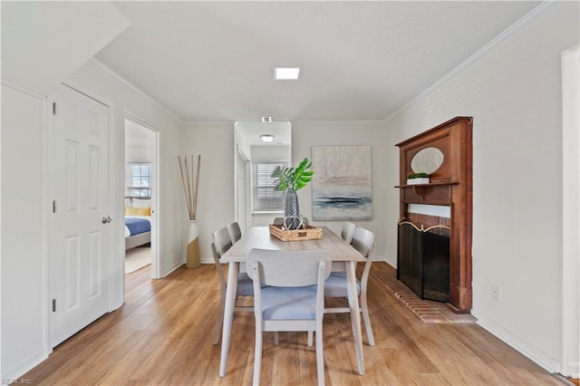 dining room with ornamental molding, a brick fireplace, baseboards, and light wood finished floors