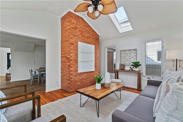 living room with lofted ceiling with skylight, a ceiling fan, brick wall, wood finished floors, and baseboards