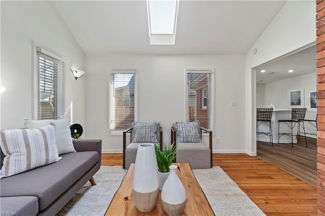 living area with vaulted ceiling with skylight, baseboards, and wood finished floors