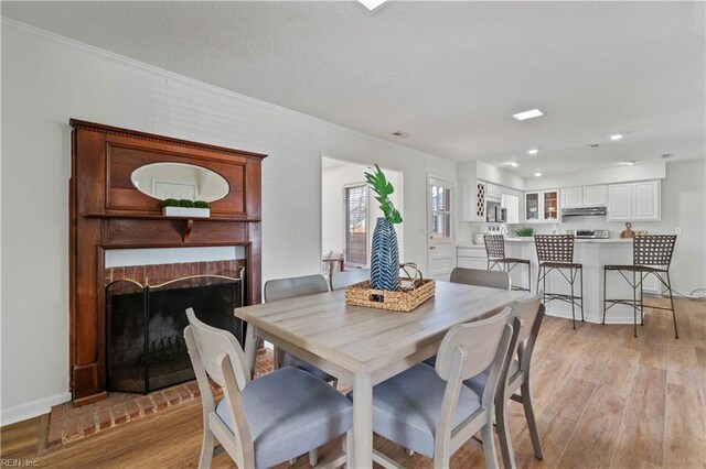 dining room featuring crown molding, recessed lighting, light wood-type flooring, and a brick fireplace