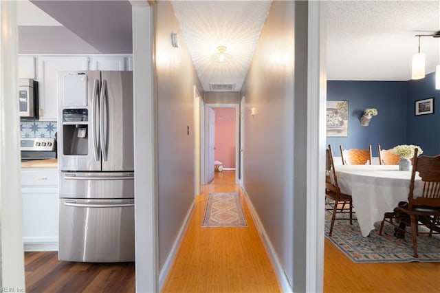 hall featuring visible vents, a textured ceiling, baseboards, and wood finished floors