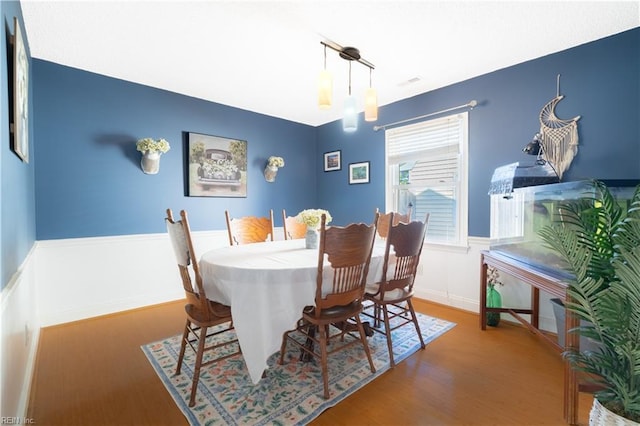 dining room with a wainscoted wall, visible vents, and wood finished floors