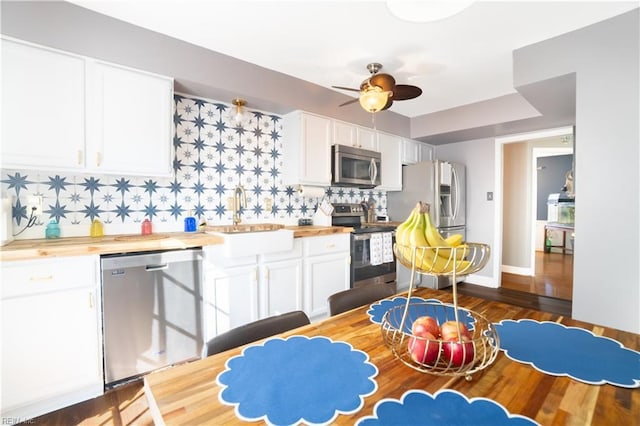 kitchen featuring a sink, butcher block countertops, stainless steel appliances, white cabinets, and backsplash