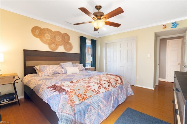 bedroom featuring wood finished floors, baseboards, ceiling fan, a closet, and crown molding