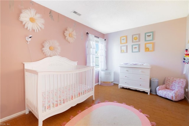 bedroom with visible vents, baseboards, a nursery area, and wood finished floors