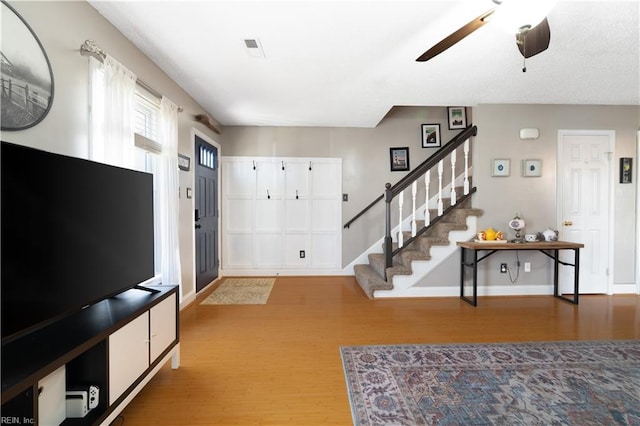 foyer entrance featuring visible vents, baseboards, ceiling fan, stairway, and wood finished floors