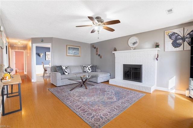 living room with a ceiling fan, a brick fireplace, light wood-style floors, and visible vents