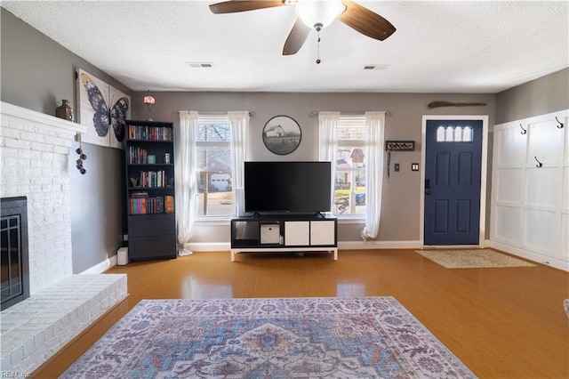 living room featuring visible vents, a brick fireplace, a textured ceiling, and wood finished floors