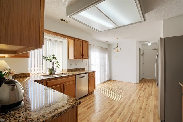 kitchen with light wood-style flooring, stainless steel appliances, a sink, visible vents, and brown cabinets