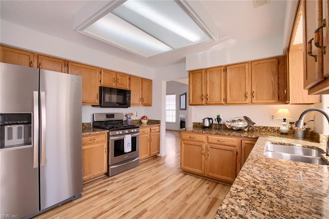 kitchen featuring stainless steel appliances, light wood-style floors, brown cabinetry, a sink, and light stone countertops