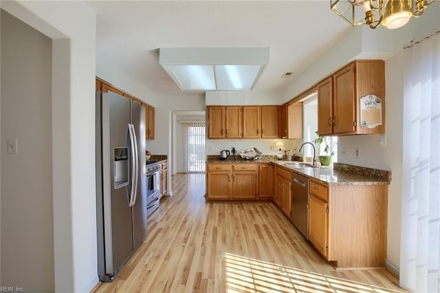 kitchen featuring stainless steel appliances, an inviting chandelier, light wood-style flooring, and brown cabinets