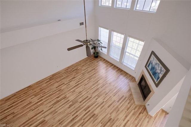 unfurnished living room with visible vents, ceiling fan, light wood finished floors, and a high ceiling