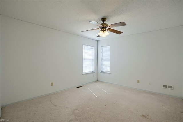 spare room featuring a textured ceiling, ceiling fan, light colored carpet, visible vents, and baseboards