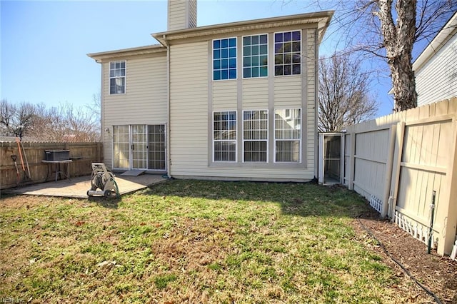 rear view of property with a chimney, a patio area, a fenced backyard, and a lawn