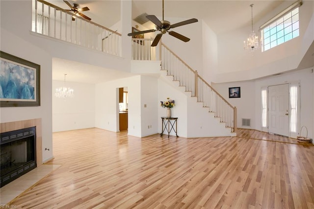 unfurnished living room with a fireplace, visible vents, stairway, light wood-style floors, and ceiling fan with notable chandelier