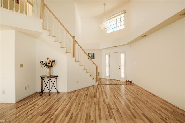 entryway featuring a towering ceiling, a notable chandelier, stairway, and wood finished floors