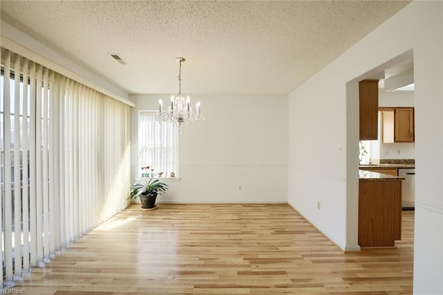 unfurnished dining area featuring a textured ceiling, a notable chandelier, visible vents, and light wood-style floors