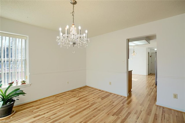 spare room featuring a notable chandelier, light wood-style flooring, and a textured ceiling