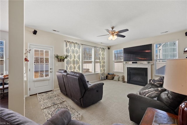 carpeted living area with a textured ceiling, ceiling fan, a fireplace with flush hearth, and visible vents