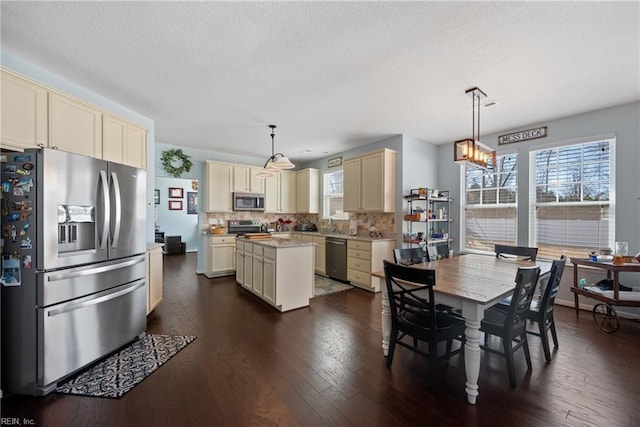 kitchen with dark wood-style floors, a center island, tasteful backsplash, cream cabinets, and appliances with stainless steel finishes