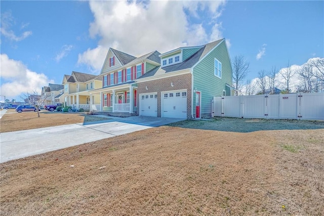 view of front facade with covered porch, concrete driveway, a front yard, a gate, and fence