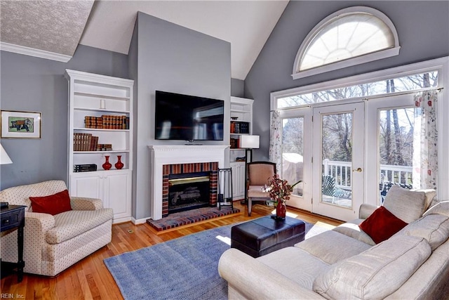 living area with lofted ceiling, a fireplace, ornamental molding, and wood finished floors