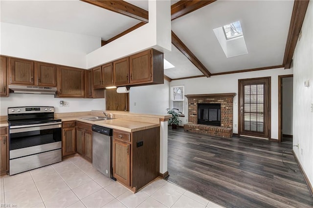 kitchen featuring under cabinet range hood, open floor plan, stainless steel appliances, light countertops, and a brick fireplace