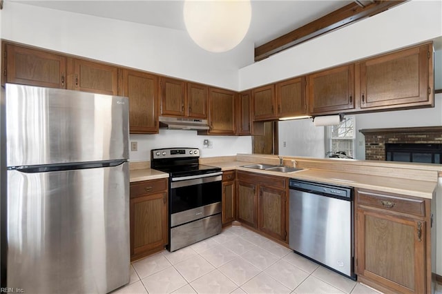 kitchen with a peninsula, a sink, stainless steel appliances, light countertops, and under cabinet range hood