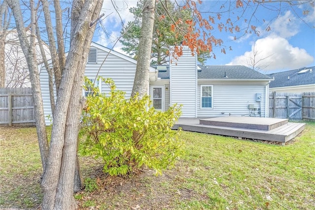 rear view of house featuring a chimney, fence, a lawn, and a wooden deck