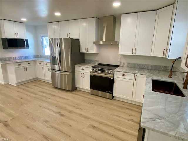 kitchen with stainless steel appliances, wall chimney range hood, a sink, and light wood-style floors