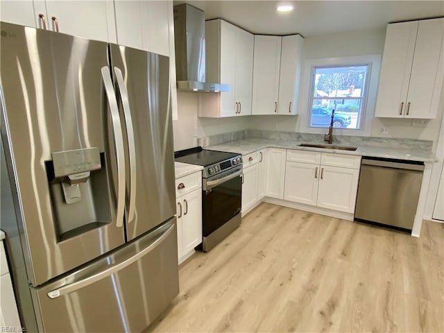 kitchen with stainless steel appliances, a sink, light wood-style floors, white cabinets, and wall chimney exhaust hood