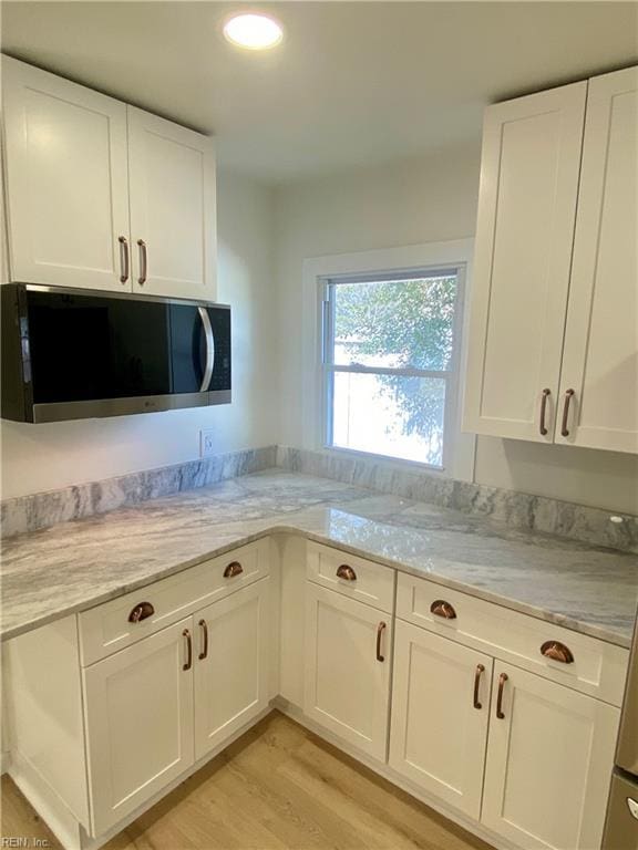 kitchen with light wood-type flooring, light stone countertops, white cabinetry, and stainless steel microwave