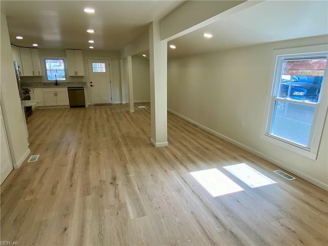 interior space featuring light wood-style flooring, a sink, baseboards, white cabinets, and stainless steel dishwasher