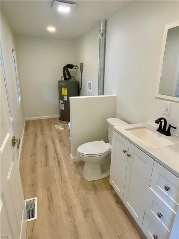 bathroom featuring toilet, electric water heater, wood finished floors, visible vents, and vanity