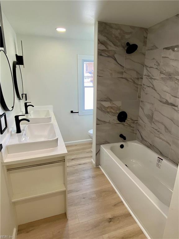 full bath with toilet, double vanity, a sink, and wood finished floors