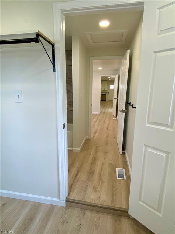 corridor with attic access, light wood-type flooring, visible vents, and baseboards