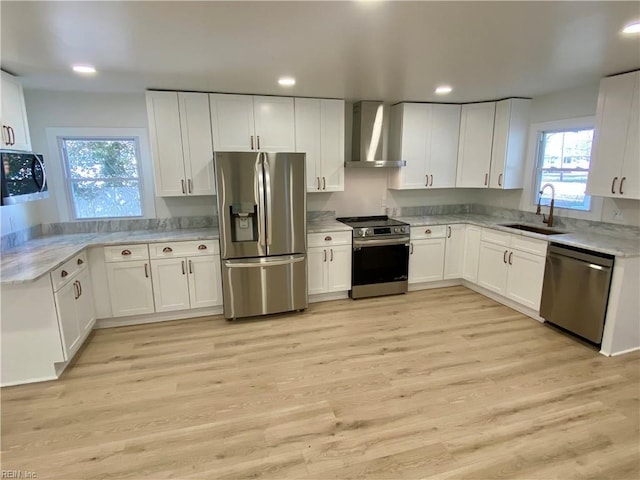 kitchen with light wood-style flooring, appliances with stainless steel finishes, wall chimney range hood, white cabinetry, and a sink