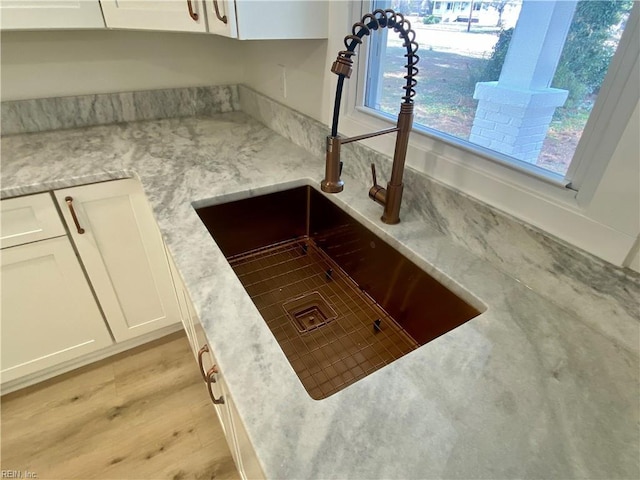 room details featuring light wood-style floors, white cabinetry, light stone counters, and a sink