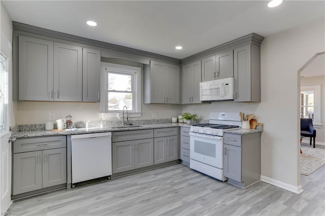 kitchen featuring arched walkways, white appliances, a sink, gray cabinets, and light wood finished floors