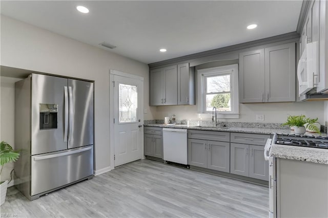 kitchen featuring light stone counters, gray cabinets, light wood-style flooring, a sink, and white appliances