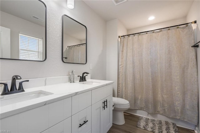 full bath with double vanity, wood finished floors, a sink, and toilet