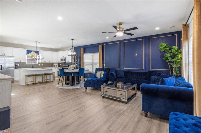 living area with recessed lighting, light wood-style flooring, and ceiling fan with notable chandelier