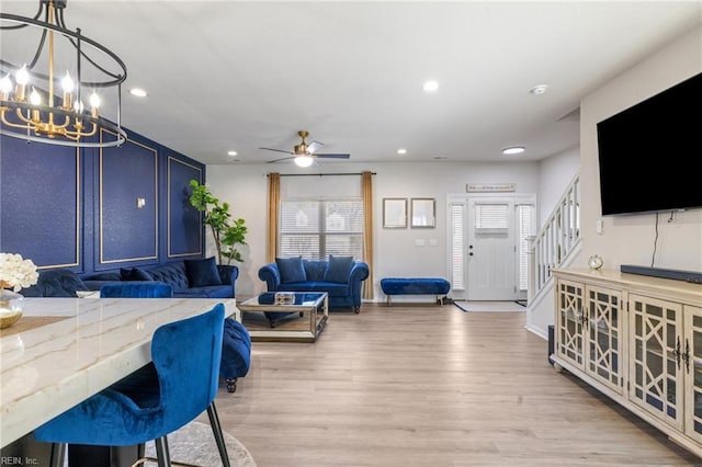 living area with recessed lighting, ceiling fan with notable chandelier, baseboards, stairs, and light wood-style floors