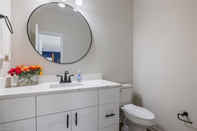 bathroom featuring a textured wall, vanity, and toilet